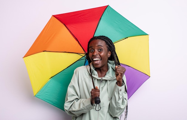 Hübsche schwarze Frau, die sich schockiert fühlt, lacht und den Erfolg feiert. Regenschirmkonzept