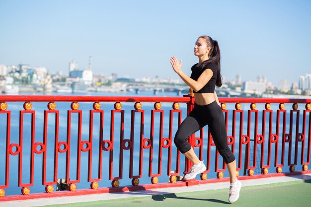 Hübsche Sportlerin in Sportbekleidung, die an der Brücke läuft. Platz für Text