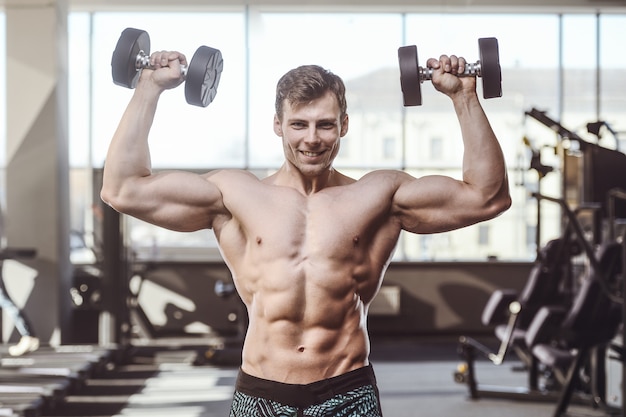 Hübsche, starke Bodybuilder-Sportler, die Muskeln mit Hanteln aufpumpen