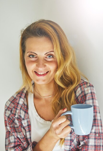 Hübsche stehende Frau, die eine Tasse Kaffee hält