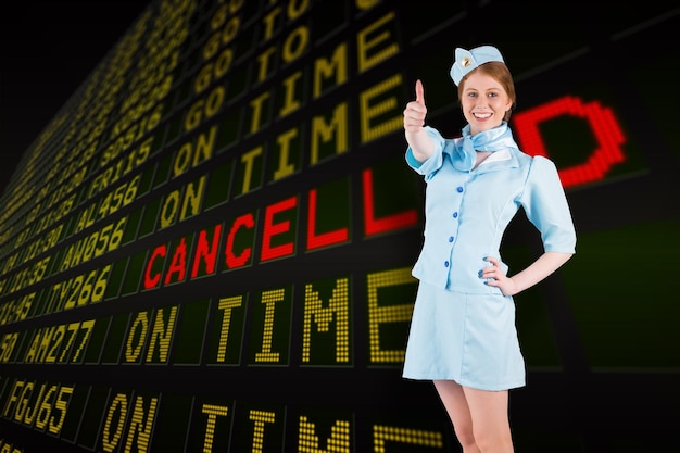 Hübsche Stewardess mit der Hand auf der Hüfte gegen die schwarze Abflugtafel des Flughafens