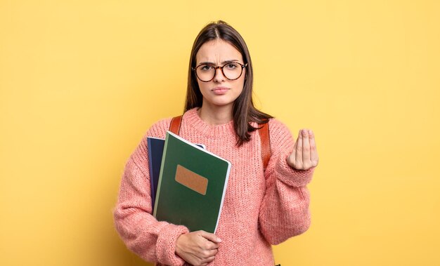 Hübsche Studentenfrau, die eine Capice- oder Geldgeste macht und Ihnen sagt, dass Sie bezahlen sollen