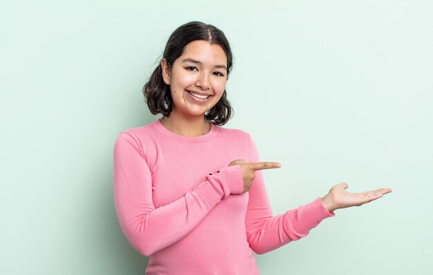 Hübsche Teenager-Frau, die lächelt, sich glücklich, sorglos und zufrieden fühlt und auf ein Konzept oder eine Idee auf dem Kopienraum auf der Seite zeigt