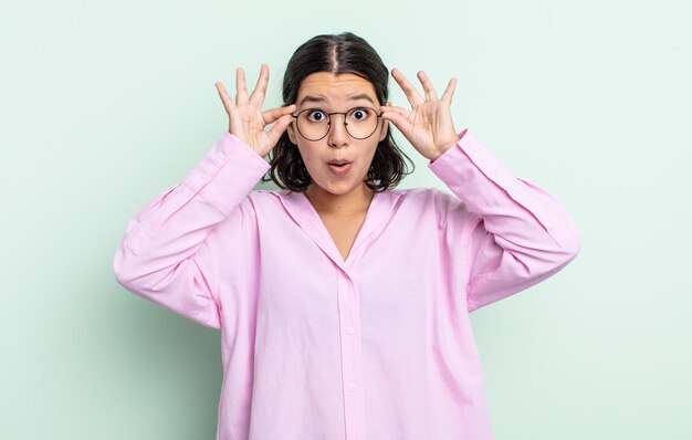 Hübsche Teenager-Frau, die sich schockiert, erstaunt und überrascht fühlt und eine Brille mit erstauntem, ungläubigem Blick hält