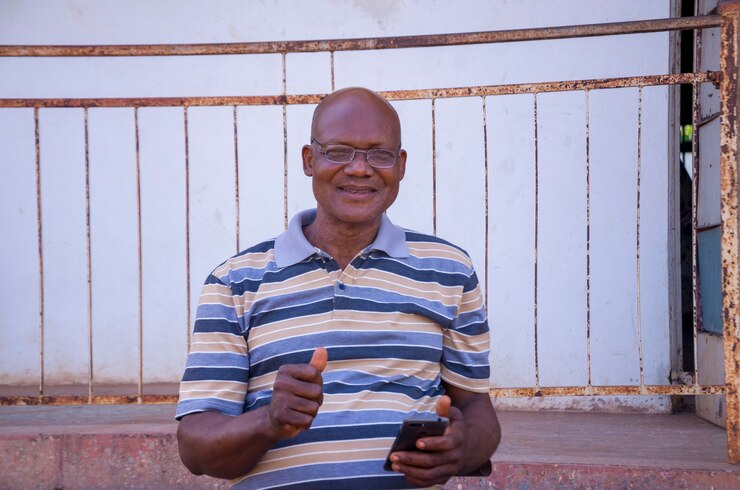 Hübscher älterer afrikanischer Mann, der Streifenkleidung trägt und sich aufgeregt fühlt, was er auf seinem Telefon gesehen hat.