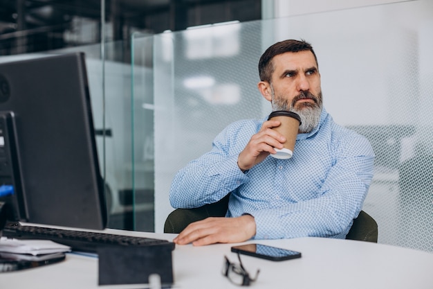 Hübscher älterer Geschäftsmann, der im Büro am Computer arbeitet