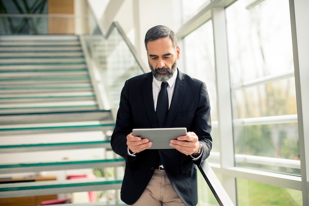 Hübscher älterer Geschäftsmann mit digitaler Tablette im modren Büro