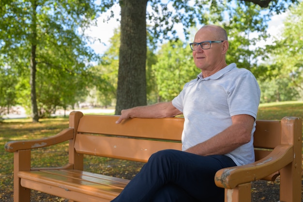 Hübscher älterer Mann, der beim Sitzen im Park denkt