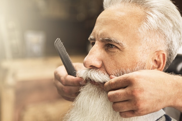 Hübscher älterer Mann, der im Friseursalon Styling und Trimmen seines Bartes erhält