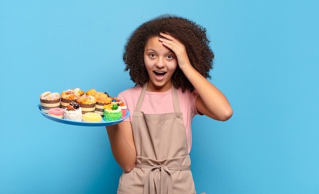 Hübscher Afro-Teenager, der glücklich, erstaunt und überrascht aussieht, lächelt und erstaunliche und unglaublich gute Nachrichten erkennt. humorvolles Bäckerkonzept