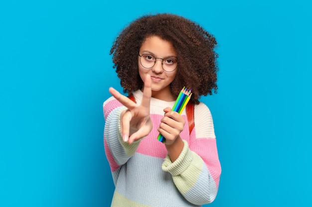 Hübscher Afro-Teenager, der glücklich, sorglos und positiv lächelt und aussieht und mit einer Hand Sieg oder Frieden gestikuliert. studentisches Konzept