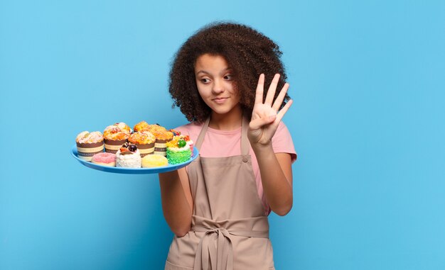 Hübscher Afro-Teenager, der lächelt und freundlich aussieht, Nummer vier oder vier mit der Hand nach vorne zeigt, herunterzählt