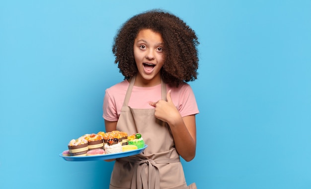 Hübscher Afro-Teenager, der schockiert und überrascht mit weit geöffnetem Mund aussieht und auf sich selbst zeigt. humorvoller Bäcker