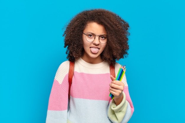 Hübscher Afro-Teenager, der sich angewidert und gereizt fühlt, die Zunge herausstreckt und etwas Böses und Glückliches nicht mag.