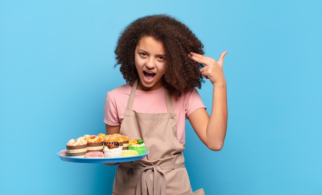 Hübscher Afro-Teenager, der unglücklich und gestresst aussieht, Selbstmordgeste, die Waffenzeichen mit der Hand macht und auf den Kopf zeigt. humorvolles Bäckerkonzept