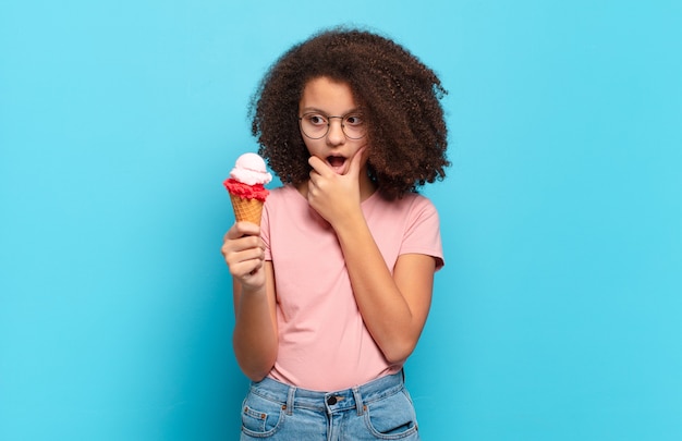 Hübscher Afro-Teenager mit offenem Mund und weit geöffneten Augen und Hand am Kinn, der sich unangenehm geschockt fühlt und sagt, was oder wow.