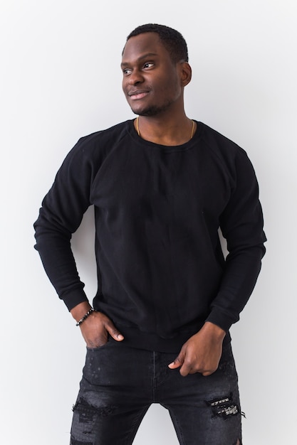 Hübscher Afroamerikanermann, der im schwarzen Sweatshirt auf weißem Hintergrund aufwirft. Jugendstraßenmode