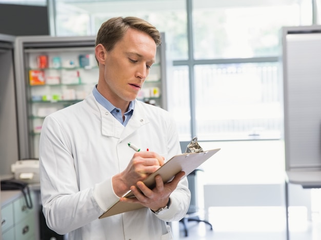 Foto hübscher apotheker, der auf klemmbrett schreibt