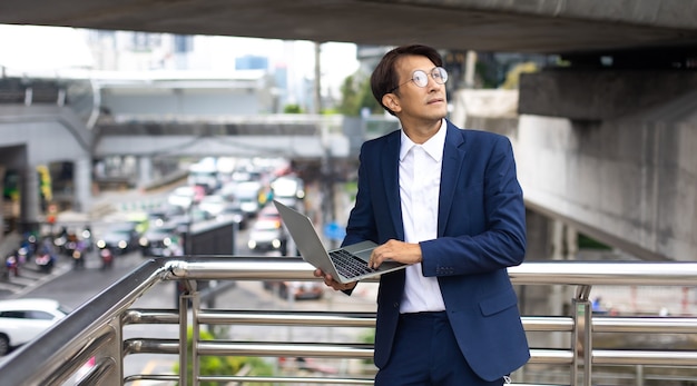 Hübscher asiatischer Geschäftsmann, der draußen mit Computer arbeitet