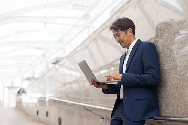 Hübscher asiatischer Geschäftsmann, der draußen mit Computer arbeitet