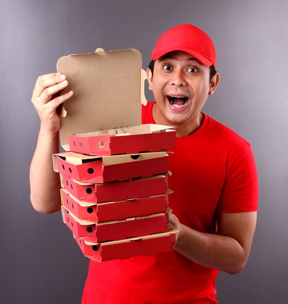 Foto hübscher asiatischer mann in der roten kappe, die italienische pizza der lebensmittelbestellung in pappkartons gibt, die im studio isoliert werden.