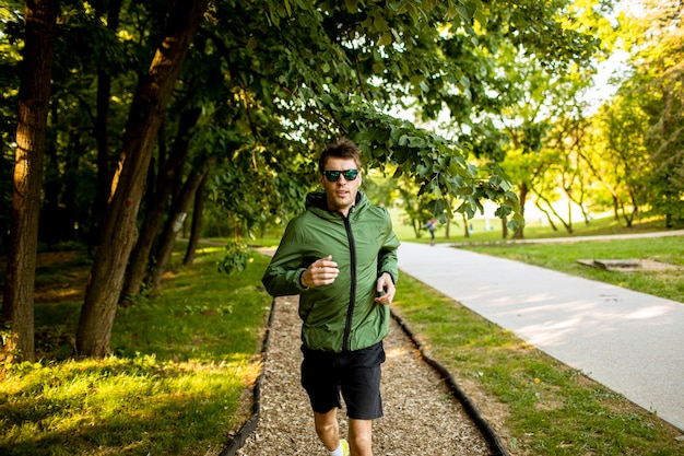 Hübscher athletischer junger Mann, der während des Trainings im sonnigen grünen Park läuft