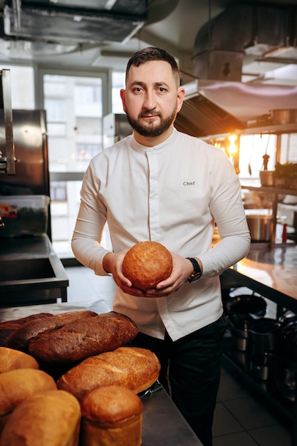 Hübscher Bäcker in Uniform, der frisch gebackenes Brot in der Bäckerei hält