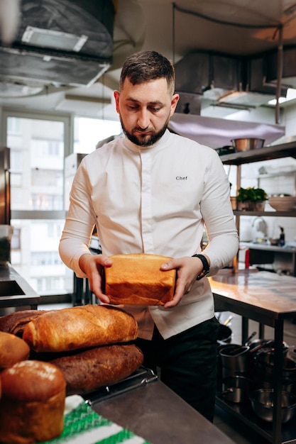 Hübscher Bäcker in Uniform, der frisch gebackenes Brot in der Bäckerei hält