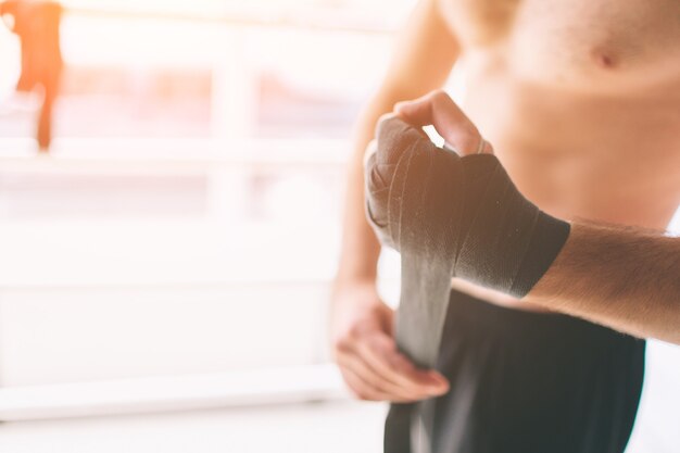 Hübscher bärtiger Boxer mit nacktem Oberkörper, der seine Hände umwickelt und bereit ist, im Kampfclub zu kämpfen