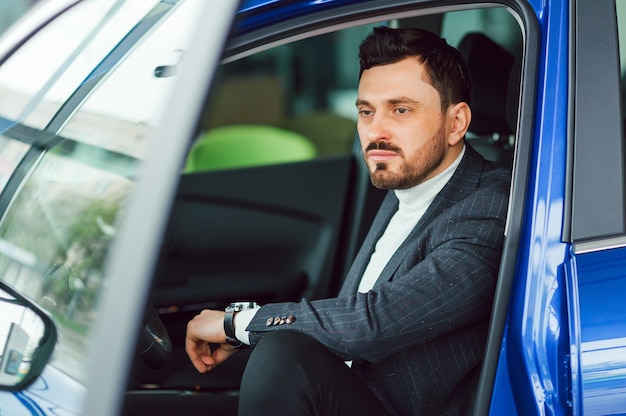 Hübscher bärtiger Geschäftsmann sitzt in einem neuen Auto im Autohaus