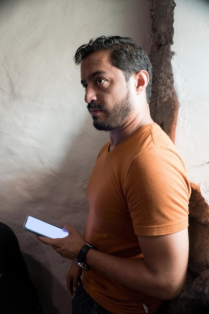 Hübscher bärtiger hispanischer Mann mit orangefarbenem T-Shirt und Smartphone