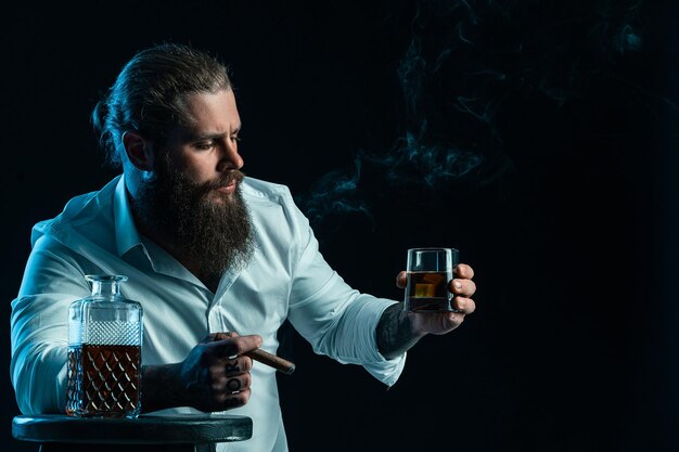 Hübscher bärtiger männlicher Rauch, eine Zigarre hält ein Glas Whisky, gekleidet in weißes Hemd Studioaufnahme