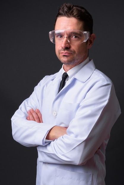 hübscher bärtiger Mann Arzt als Wissenschaftler mit Schutzbrille gegen graue Wand