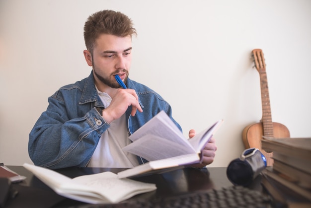 Hübscher bärtiger Mann, der am Tisch sitzt und Bücher liest. Mann beschäftigt sich mit Selbstbildung zu Hause.