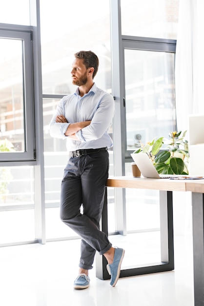 Hübscher bärtiger Mann im Büro, der nahe Tisch steht