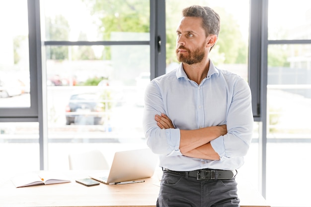 Hübscher bärtiger Mann im Büro, der nahe Tisch steht