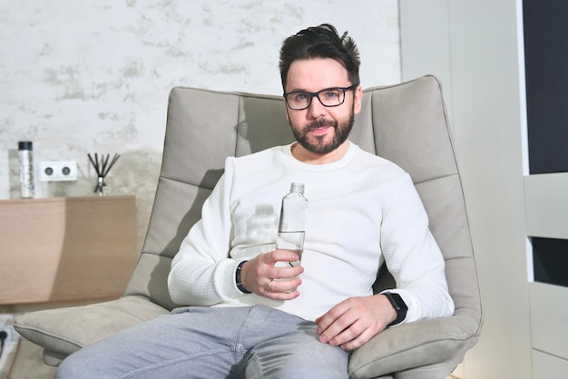 hübscher bärtiger mann in brille junge person trinkt reines wasser aus plastikflasche zu hause