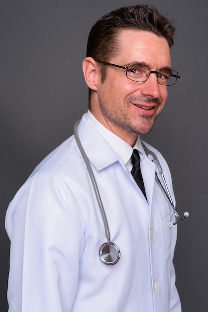 hübscher bärtiger Mannarzt mit Brille gegen graue Wand
