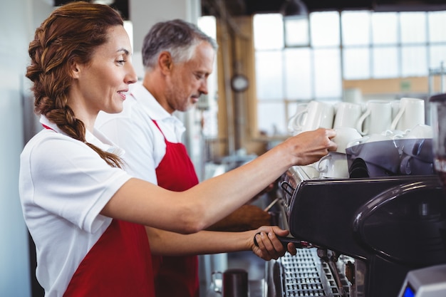 Hübscher Barista, der die Kaffeemaschine mit Kollegen hinten verwendet