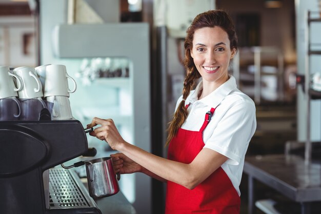 Hübscher Barista, der Kamera betrachtet und die Kaffeemaschine verwendet