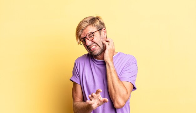 Hübscher blonder erwachsener Mann, der sich gestresst, frustriert und müde fühlt, schmerzenden Nacken reibt, mit einem besorgten, unruhigen Blick