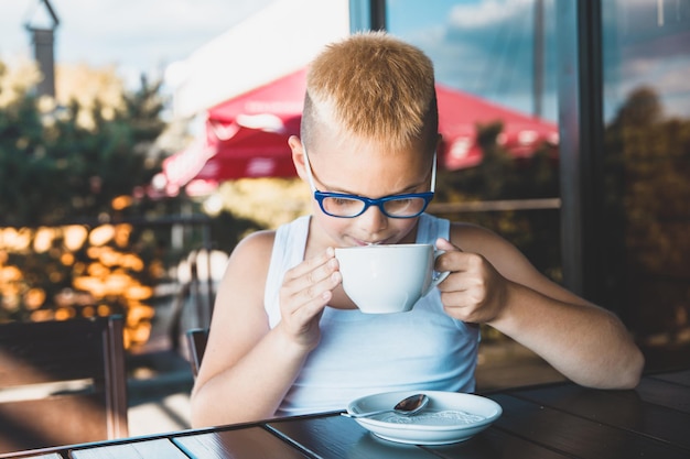 Hübscher blonder Junge in einem weißen T-Shirt in einem Restaurant, das Kaffee trinkt