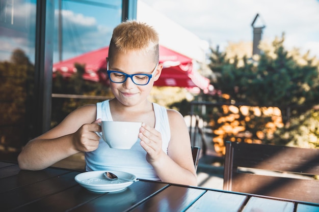 Hübscher blonder Junge in einem weißen T-Shirt in einem Restaurant, das Kaffee trinkt