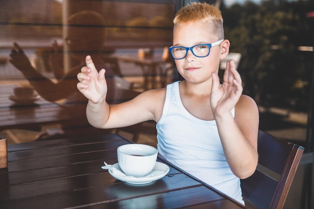 Hübscher blonder Junge in einem weißen T-Shirt in einem Restaurant, das Kaffee trinkt