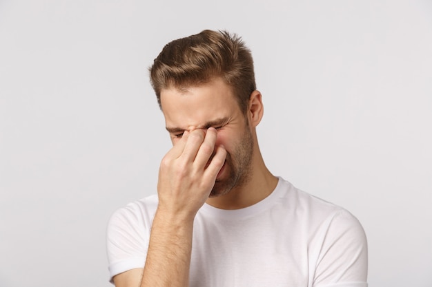 Hübscher blonder Kerl mit blauen Augen und weißem T-Shirt, das Müdigkeit und Bedrängnis glaubt