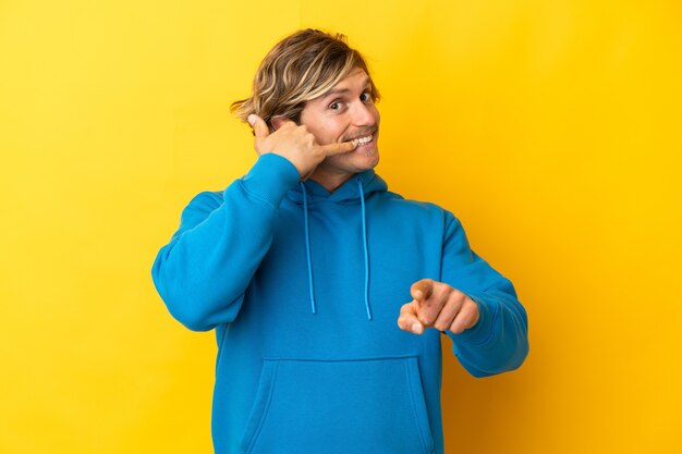 Hübscher blonder Mann lokalisiert auf Gelb, der Telefongeste macht und nach vorne zeigt