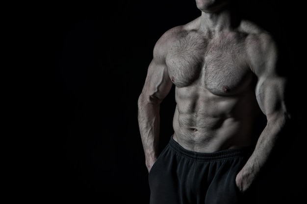 Hübscher Bodybuilder oder sexy muskulöser Kerl mit Sportlerkörper, Torso und Brusttrainingssport und posiert im Fitnessstudio auf schwarzem Hintergrund, Kopierraum