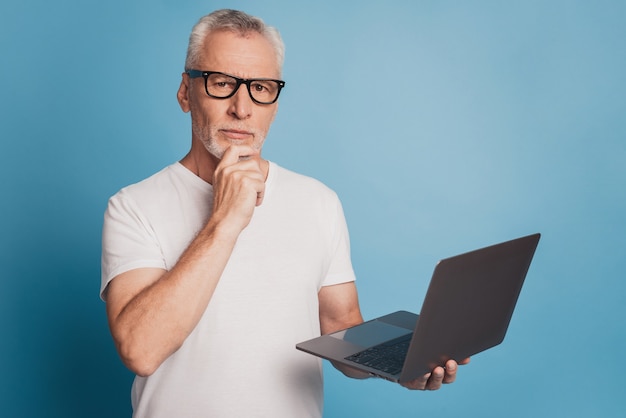 Hübscher Brainstorming alter Mann mit Laptop auf blauem Hintergrund isoliert
