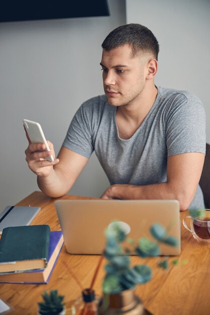 Hübscher brünette Mann, der online mit Laptop in gemütlicher Atmosphäre arbeitet, während er jemanden auf dem Handy anruft