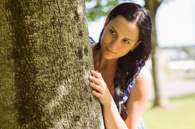 Hübscher Brunette, der an einem Baum sich lehnt